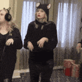 a woman wearing a cat hat and ear muffs is dancing in front of a window