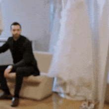 a man in a suit is sitting on a couch next to a white dress .