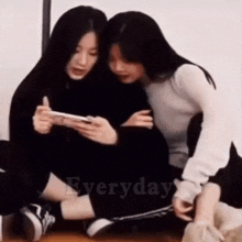 two girls are sitting on the floor looking at a cell phone and the word everyday is on the bottom