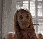 a woman is smoking a cigarette in front of a window in a room .
