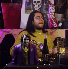 a man with long hair is sitting at a table with a bottle of beer and a joker statue