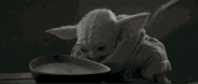 a baby yoda is eating from a bowl of food .