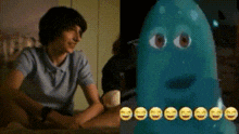 a man is sitting at a table next to a blue ghost with smiley faces on its face .