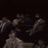 a group of people sitting in a dark room with a man wearing a badge that says ' l.a. '