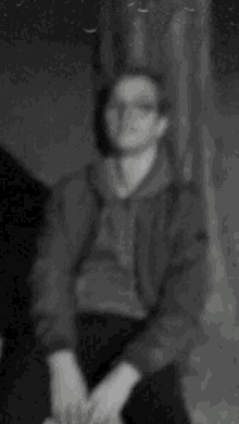 a blurry picture of a man sitting in front of a tree in a dark room .