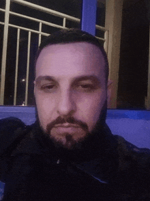 a man with a beard looks at the camera in front of a blue window