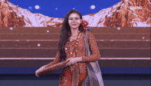 a woman with a flower in her hair is on a stage in front of a screen that says grandtv