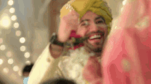 a man in a turban is holding a rose in his mouth while standing next to a woman in a pink dress .