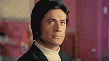 a man in a black suit and white turtleneck looks to his left