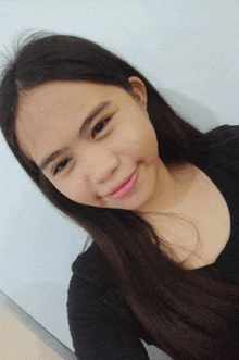 a girl with long dark hair is smiling and wearing a black shirt