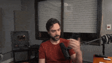 a man in a red shirt is sitting in front of a microphone holding a cell phone
