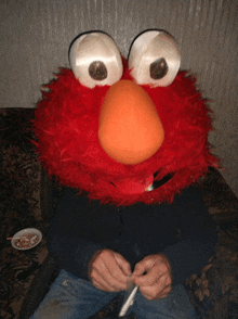 a man is sitting on a couch with a stuffed elmo on his head