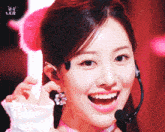 a close up of a woman wearing earrings and a microphone with a pink background