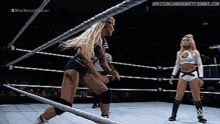 two women are wrestling in a wrestling ring and one of them is wearing shorts and knee pads .