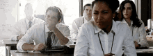 a group of people are sitting at desks in a classroom and one of them is covering her mouth with her hand .