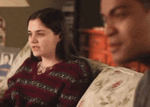 a man and a woman are sitting on a couch and the woman is wearing a red sweater
