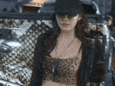 a woman wearing a black hat and a leopard print crop top stands in front of a truck
