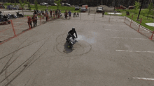 a man riding a motorcycle in a parking lot with people watching