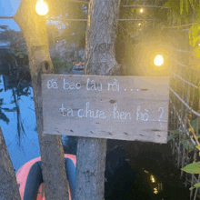 a wooden sign hanging from a tree that says da bao lau roi ta chua hen ho