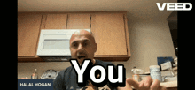 a bald man says " you " in front of a kitchen