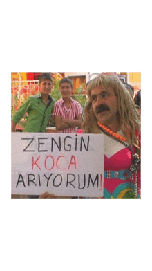 a man in a wig holds a sign that says " zengin koca ariyorum "