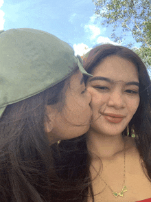 a woman kissing another woman on the cheek while wearing a green hat