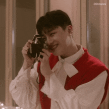 a man in a red vest is taking a picture with a camera and smiling