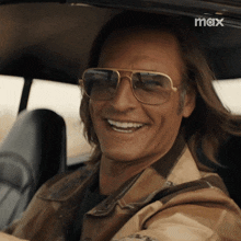 a man wearing sunglasses is smiling while sitting in a car with a max logo in the background