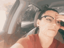 a woman wearing glasses is sitting in a car and touching her forehead