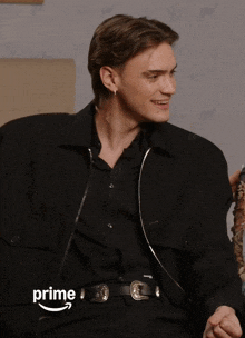 a man in a black jacket is sitting on a couch with the word prime on the bottom