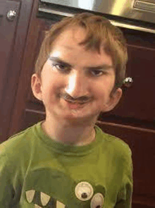 a young boy with a fake mustache is wearing a green shirt with a monster on it .