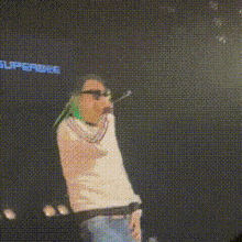 a man with green hair is singing into a microphone in front of a blue background