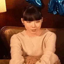 a woman is sitting on a couch with balloons in the background and smiling .