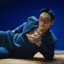 a man with a tattoo on his chest is laying on the floor wearing sunglasses and a blue suit