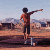 a boy in an orange shirt is standing on one leg in the desert