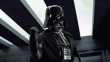 darth vader from star wars is wearing a helmet and making a fist .