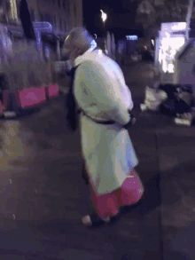 a man in a white coat and red skirt is walking down a street