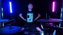 a man wearing a shirt with the letter j on it stands in front of a drum set