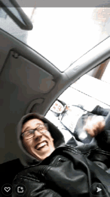 a man wearing glasses and a hooded jacket is sitting in a car