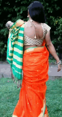a woman in an orange saree and a green striped blouse is walking on the grass .