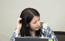 a woman in a plaid shirt is sitting in front of a laptop and asking " sometimes "