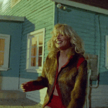 a woman in a fur coat is sitting in front of a blue house