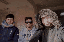 three young men are posing for a picture and one of them is wearing a camfed sweatshirt