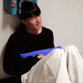a man in a black sweater sits on the floor holding a blue blanket