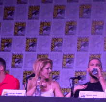 a group of people sitting at a table with a comic con sign behind them