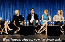 a group of people are sitting on a stage and one of them says well i mean okay so now i 'm single