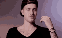 a young man with a tattoo on his chest is wearing a baseball cap and a black shirt .