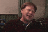 a man is laughing in a living room while wearing a red shirt .