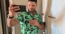 a man in a green shirt with question marks on it takes a selfie with his phone