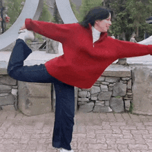 a woman in a red sweater and blue jeans is standing on one leg